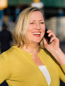 Author Tina Larsson - blond white woman with a big smile wearing a yellow sweater and holding a phone