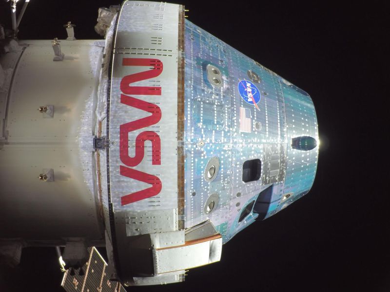 A closeup view of what looks like the nose of the rocket. It is shiny silver on the cone and painted white with NASA in red letters on the body.