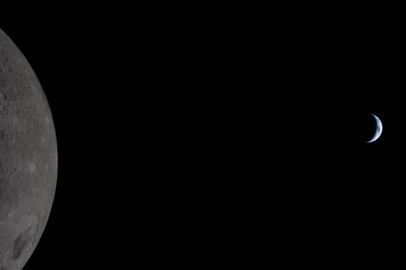 A large segment of the moon at the leftmost side of the frame and a tiny Earth as a crescent at the rightmost edge. Most of the image is of the black space between them, emphasizing the perceived difference in size.